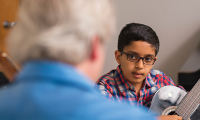 A young guitar student looks to their instructor