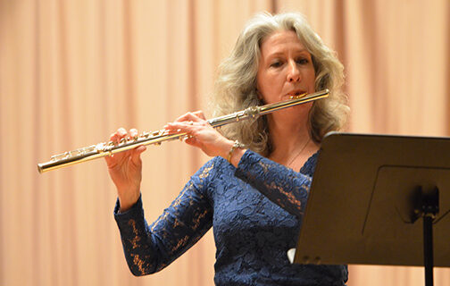 An adult student plays the flute on stage