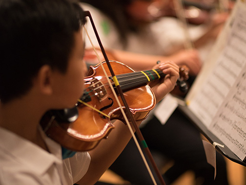 A young student plays the violin from sheet music during an ensemble performance