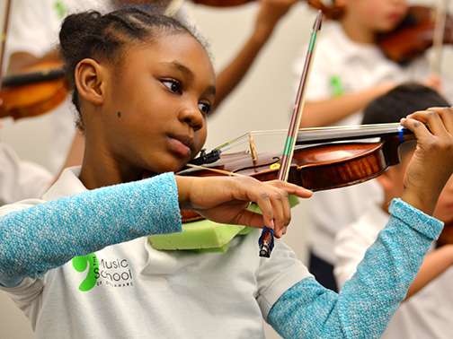 A young student playing violin with other Suzuki Academy students